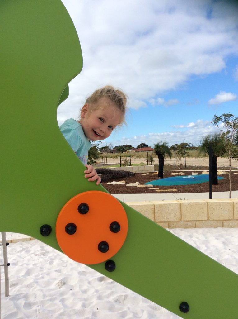 smiling child on Proludic play equipment slide against blue sky
