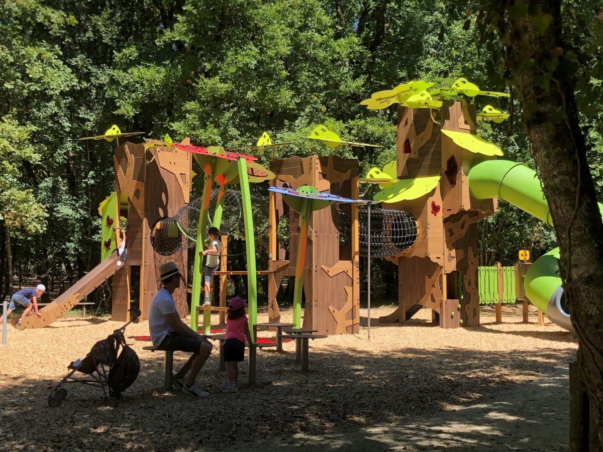 The nature themed play structure at Zoodyssée animal park. A large brown multiplay structure decorated with green leaf designs, with climbing and crawling zones and a large green covered slide.