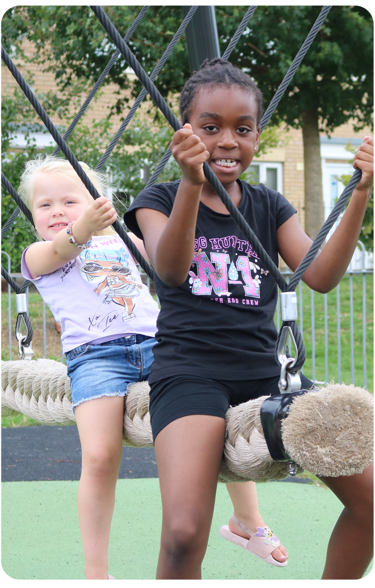Two young girls swing on our rope swing with big smiles on their faces, looking at the camera.